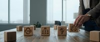 Business professional arranging wooden blocks with corporate icons on office desk representing strategic planning and organizational development concepts.