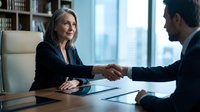 Professional mature businesswoman shaking hands with male colleague in modern office setting during successful meeting or negotiation.