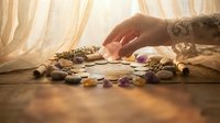 Fortune teller woman reading future with colorful gemstones and crystals on wooden table in warm sunlight for spiritual guidance and divination.