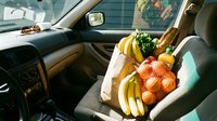 Fresh groceries in reusable shopping bag on car passenger seat after supermarket trip. Healthy food shopping concept with fruits and vegetables.