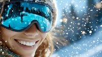 Cheerful female skier with bright smile wearing blue reflective goggles capturing winter mountain landscape reflection during snowfall, close up portrait in snowy weather.