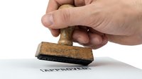 Caucasian male hand pressing wooden rubber stamp with approved text on white paper document, isolated background.