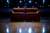 Brown velvet couch on wooden floor against dark background with blue bokeh lights creating dramatic atmosphere for interior design and theatrical staging.