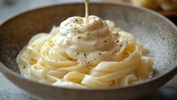 Creamy fettuccine pasta topped with whipped ricotta cream and black pepper, drizzled with golden olive oil in ceramic bowl, macro food photography.