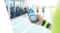 Athlete holding smartphone with fitness app in modern gym, tracking workout progress and health data for active lifestyle.