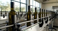 Industrial olive oil bottling line with green glass bottles moving on automated conveyor system in modern food processing facility.