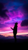 Silhouette of person standing with outstretched hand against vibrant purple and pink sunset sky, mountains in background creating spiritual, peaceful atmosphere.