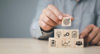 Business professional arranging wooden blocks with strategy icons including target, lightbulb, gears, and growth chart on desk for planning concepts.