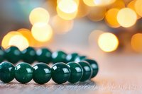 Green jade beads bracelet on wooden surface with soft golden bokeh lights in background creating magical atmosphere for wellness and spiritual concepts.
