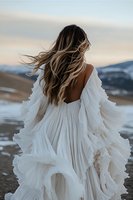 Young woman in flowing white dress with long blonde hair standing against mountain landscape, wind dramatically moving fabric and hair in romantic outdoor scene.