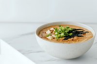 Creamy miso soup garnished with fresh green onions and nori seaweed in white ceramic bowl on marble surface, traditional Japanese cuisine styling.