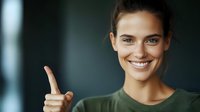 Young Mediterranean woman with bright smile pointing finger at camera wearing green sweater against dark blurred background, positive friendly expression.