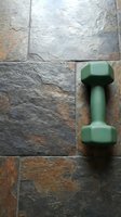 Green dumbbell resting on rustic slate tile surface with natural stone texture, suitable for fitness, wellness, and gym-related design projects.