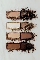 Crushed makeup powder swatches in various brown and nude shades on white marble background, showing texture and pigment intensity for cosmetic product photography.