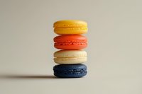 Stack of colorful French macarons in yellow, coral, white and navy blue on neutral background, minimalist food photography composition for bakery marketing.