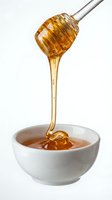Golden honey dripping from a dipper into a white ceramic bowl, showcasing rich texture and natural sweetness for food and health concepts.
