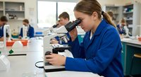 Young female scientist in blue lab coat using microscope in modern laboratory for research and analysis work.