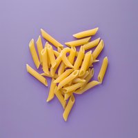 Uncooked yellow penne pasta arranged in heart shape on purple background, overhead view. Modern food styling for cooking and recipe concepts.