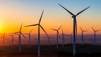 Wind turbines generating renewable energy at sunset with golden sky and mountain landscape for sustainable power concepts.