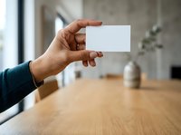 Male hand holding blank white card in modern office workspace with wooden table and blurred background, suitable for business branding and corporate mockup presentations.