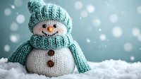 Adorable knitted snowman with mint green hat and scarf sitting in artificial snow against soft blue background with bokeh lights for winter holidays.
