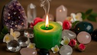 Green candle burning with smoke surrounded by healing crystals gemstones and rose petals on wooden surface for meditation spiritual wellness rituals.