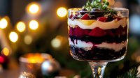 Layered berry trifle dessert in glass with whipped cream, fresh berries and chocolate crumbs against blurred festive lights background.