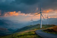 Wind turbines on mountain ridge at sunset with dramatic stormy sky, winding road, and layered mountain landscape in background.