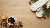 Warm winter beverage with knitted mittens, evergreen branches, cinnamon sticks, dried citrus slices, and candle on wooden surface for seasonal holiday styling.