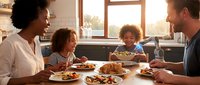 Happy mixed-race family enjoying breakfast together in modern kitchen with natural sunlight streaming through window creating warm atmosphere.
