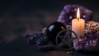 Mystical altar setup with pentagram pendant, burning candle, amethyst crystals, dried lavender and sage bundles creating spiritual witchcraft atmosphere.