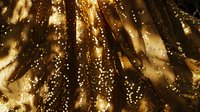 Luxurious gold liquid texture with sparkling glitter particles and flowing metallic waves creates dramatic abstract background for luxury designs and festive layouts.