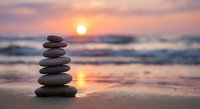 Balanced stone stack on beach at sunset with golden sky reflection in wet sand creating peaceful meditation and wellness atmosphere for relaxation concepts.