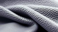 Macro shot of textured white leather material with soft folds and ripples creating an abstract pattern of light and shadow. Suitable for luxury fashion and upholstery backgrounds.