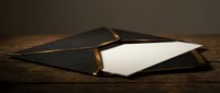 Elegant black envelope with gold trim on rustic wooden surface, white blank card inside, luxury correspondence concept for invitations.