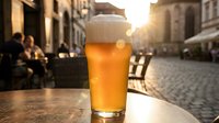 Fresh golden beer with white foam head on outdoor cafe table during sunset in historic European city street with cobblestones and warm evening light.
