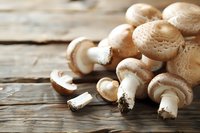 Fresh white champignon mushrooms scattered on rustic wooden table with natural lighting, macro food photography for restaurant menus and cooking blogs.