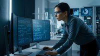 Professional female software developer coding on multiple monitors in modern tech office environment late night programming session.
