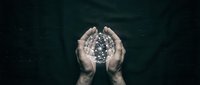 Hands holding glowing digital sphere with particle effects against dark background, representing technology, innovation, data protection, and digital transformation concepts.