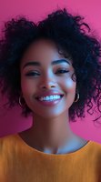 Young woman with natural curly hair smiling brightly against pink background, wearing yellow top and hoop earrings. Vibrant portrait showcasing genuine joy and confidence.
