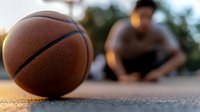 Basketball on outdoor court with blurred player in background during golden hour light. Sports equipment ready for streetball game and athletic training.