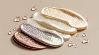Luxurious cosmetic cream swatches in metallic gold, silver, and bronze tones with water droplets on beige background, showcasing skincare product texture.