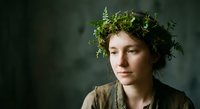 Young woman with natural green foliage crown wreath portrait against dark moody background for organic beauty wellness spa botanical concepts.