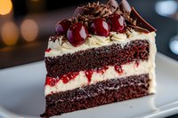 Decadent chocolate cake slice layered with cream cheese frosting and fresh cherries, topped with chocolate shavings and cherry sauce on white plate with bokeh background.