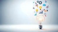 Glowing light bulb with colorful business icons floating above representing innovation, creativity, and strategic planning for corporate success.