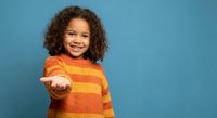 Happy mixed race girl with curly hair extending hand in welcoming gesture wearing orange striped sweater against blue background for childhood concepts.