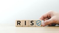 Hand placing wooden blocks spelling RISK with checkmark shield symbol representing business risk management and security assessment strategies.