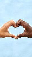 Two diverse hands forming a heart shape together against a soft blue background, symbolizing unity, love, and inclusion.