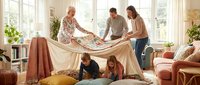 Multi-generational family building blanket fort together in bright living room. Grandparents, parents and children creating cozy play space at home.