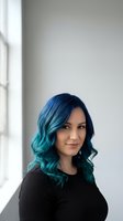 Young woman with vibrant blue-green ombre hair wearing black top in modern interior with natural window light for lifestyle and beauty content.